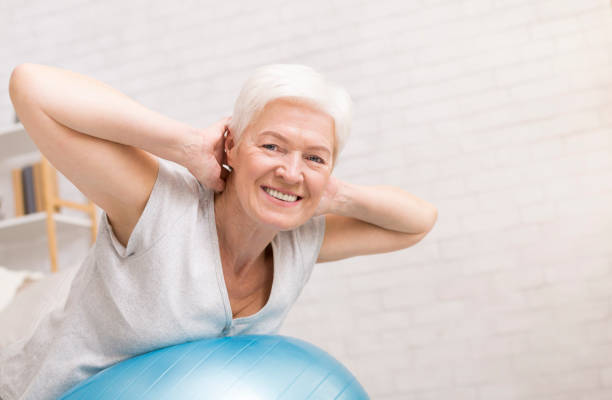 Happy Active Mature Woman Doing Exercises With Fitness Ball At Home, Free Space